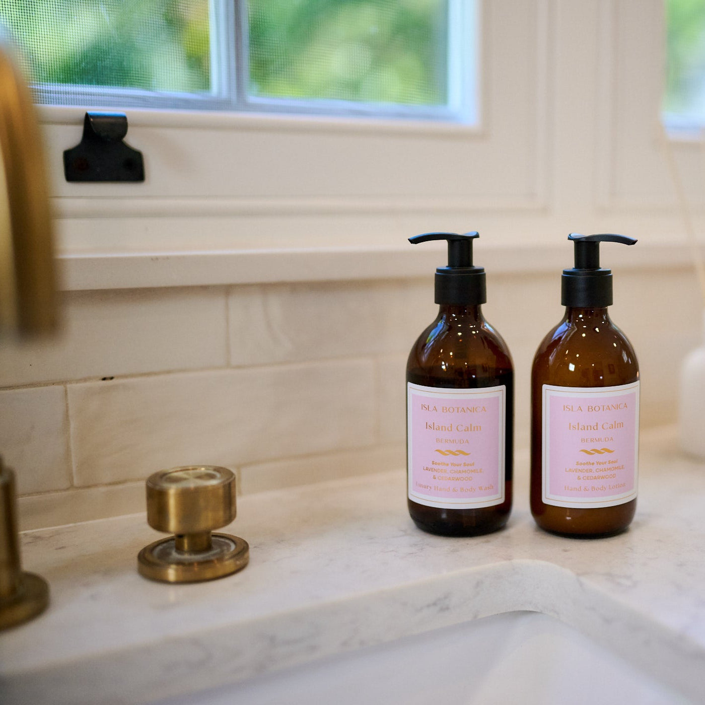 Two bottles with pink labels on a bathroom counter with a window in the background.