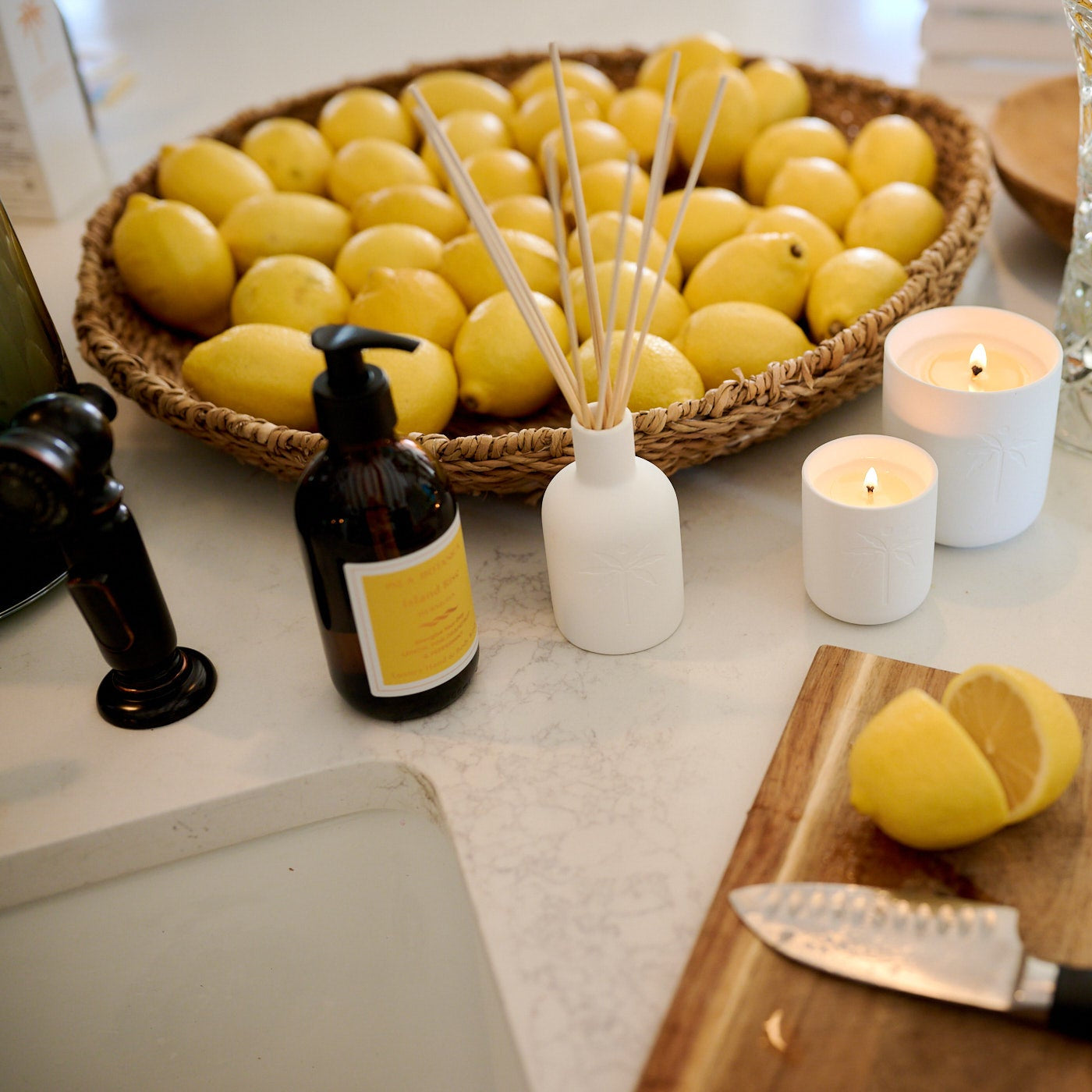 Lemons on a cutting board with candles, essential oils, and a knife on a kitchen counter.